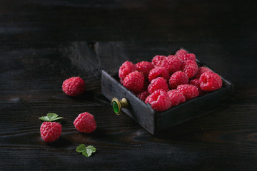 Fresh organic wet ripe raspberries in black wood box over wooden burnt background. Space for text