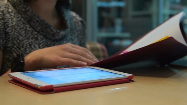 Businesswoman in cafe working with papers and making notes in tablet computer