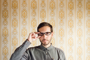 Clever geek portrait against hipster retro background. Smart casual young man wearing glasses.