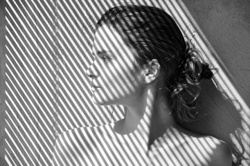 Black and white portrait of a young European girl in profile against a grunge wall with a striped shadow from the blinds.