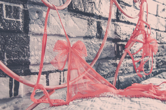 Human passion concept. Erotic red lingerie in the bedroom with a forged bed and a brick designer decorative wall. 