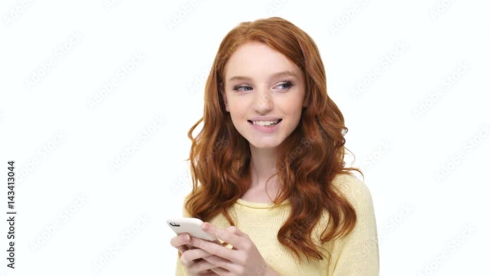 Wall mural smiling lovely girl with long red curly hair sending love message on mobile phone over white