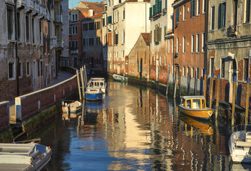 Venetian city landscape at sunset. Moored boats along the canal shore.