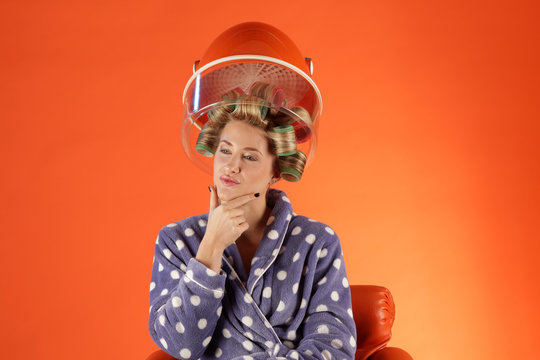 Frau f&ouml;hnt Dauerwelle mit Lockenwickler unter Trockenhaube