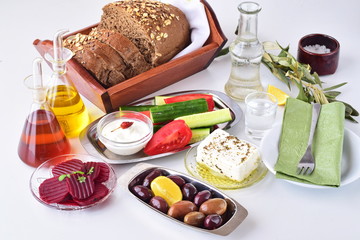Greek food, mezedes. Jars with olive oil and vine vinegar, olives,feta, tzatziki, dark bread, raki, beetroot, fresh cucumber and tomato on a white background. Healthy eating concept. Healthy food.