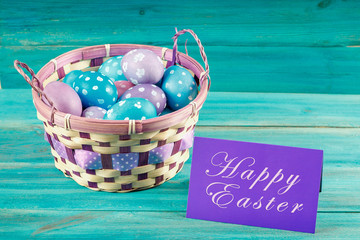 Violet and blue Easter eggs in a basket with a card. Blue wooden background. Happy easter.