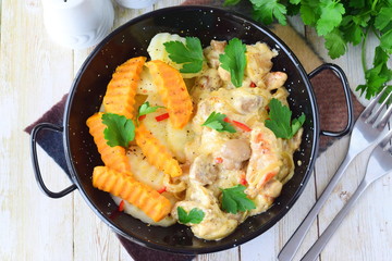 Chicken with mushrooms in a creamy souce with fried sweet potato in a black metal bowl on a wooden background. Healthy eating concept. Mediterranean lifestyle.