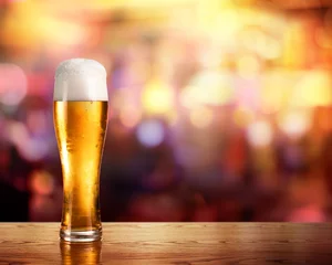 Photo sur Plexiglas Bière Bière dorée en verre avec des lumières de bar en arrière-plan