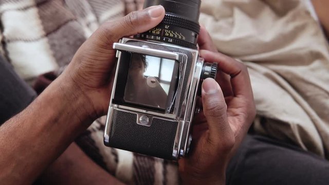 Close-up view of african man holding old photocamera, taking photo portrait beautiful woman. Multiracial couple on bed.