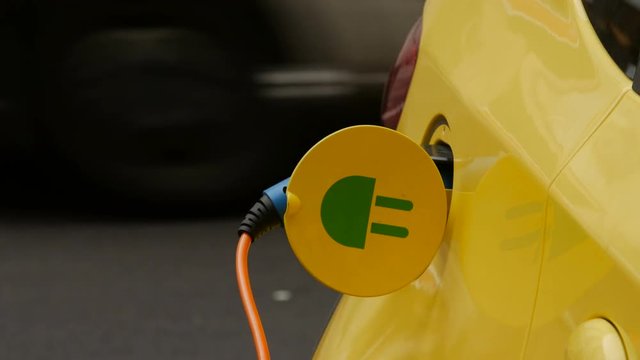 Close up of an yellow Electric Vehicle's plugged in charge port.