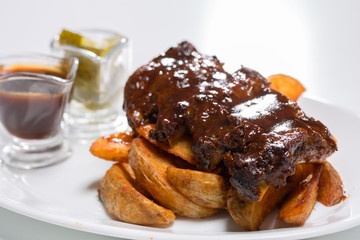 Tasty pork ribs with sauce and cucumbers on a plate