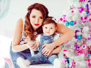 Woman hugs from behind smiling little child before Christmas tree