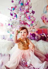 Girl in golden dress plays before pink and white Christmas tree