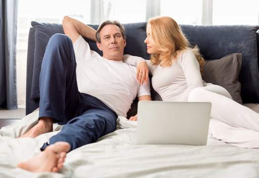 Happy Middle Aged Couple Using Laptop And Lying On Bed At Home