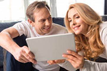 Fototapeta premium Happy middle aged couple using digital tablet at home