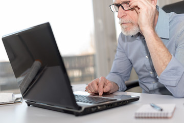 Portrait of senior businessman working on laptop, hard light