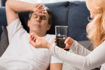 Blonde woman holding glass with water and giving medicine to sick man
