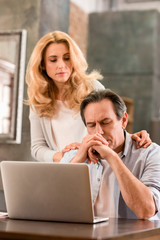 Fototapeta na wymiar Blonde middle aged woman looking at upset husband using laptop at home