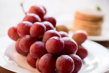 close up view of fresh red grapes on plate, pancakes behind