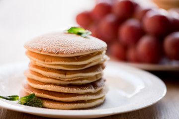 Tasty pancakes with mint and powdered sugar on white plate