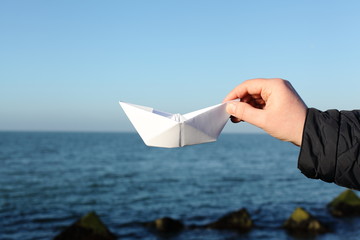 Simple paper boat in male hand. Waves and blue sky on the background. Concept of art, travelling...