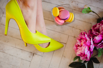 Woman's legs in yellow shoes lie on wooden floor with flowers and macaroons