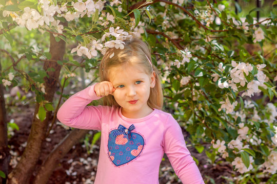 Portrait of a girl in flowers. A blonde girl in a pink dress with a heart is near of the branches of a blossoming Apple tree. Spring portrait of a child