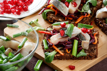 Bruschetta on rye bread with fried straws of beet and carrots, greens and slices of herring on a...