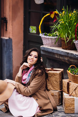 Woman in beige coat sits on the ground before table with flowerpots