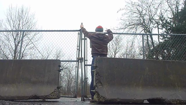 Man with skateboard jumps over cyclone fence and enters private property.
