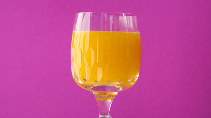 glass of orange juice with pink background.