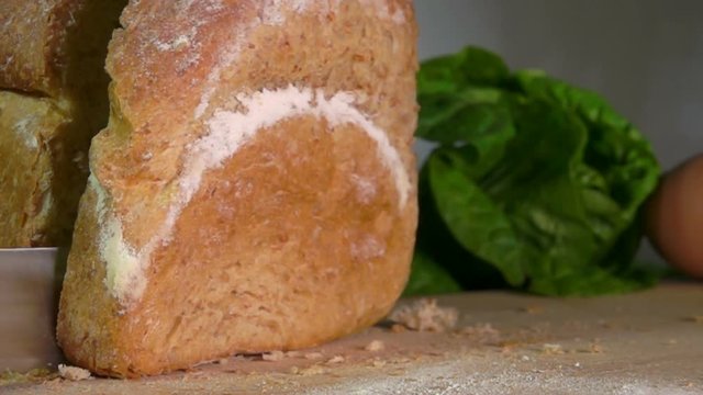 Piece of bread cut from a loaf falls on a wooden board in slow motion