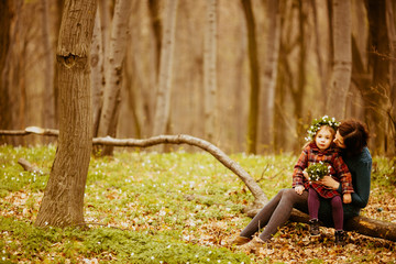 The mother with daughter sitting on the trunk and keeping a bouquet