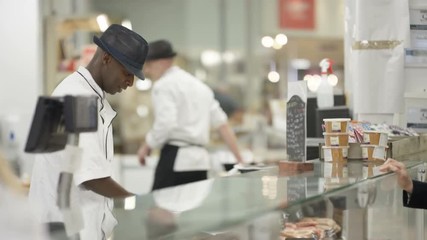 Happy worker on supermarket deli counter serving customers with a smile