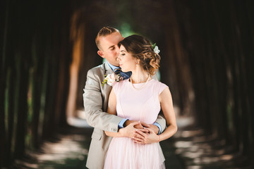 Man kisses from behind pretty woman in elegant bright dress