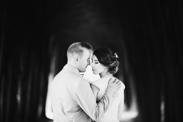 Strong man holds his hand on bride's shoulder posing with her in the forest