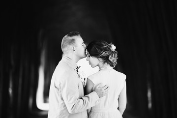 Groom holds his hand on bride's shoulders kissing her forehead