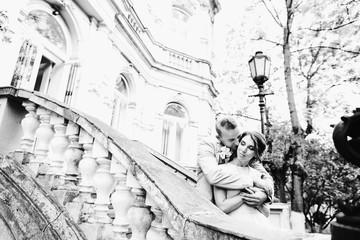 Groom hugs bride from behind standing on stone stairs of an old house