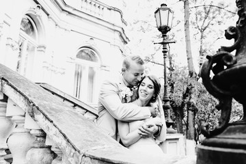 Blond groom hugs bride from behind standing with her on the stairs to old European house