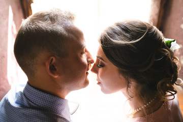 Sun shines over faces of lovely newlyweds sitting before the window