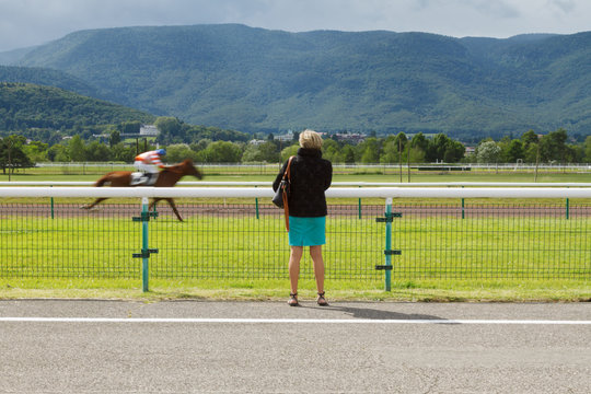 Horse racing. The woman at the racetrack looks at the galloping horses. Shot of a man without a face standing with his back