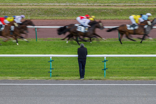 Horse racing. The man at the racetrack looks at the galloping horses. Shot of a man without a face standing with his back