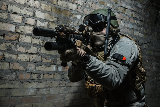 Special forces operator pointing weapon in the dark. Combat helmet, tactical radio system with folding antenna are on. Low key image