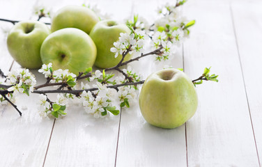Ripe green apples with spring flowers on a white wooden background.