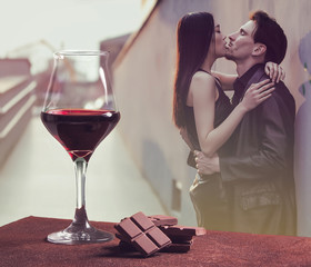 Red wine glass with chocolate and couple kissing in the city