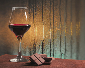 Red wine glass with chocolate and rainy windowpane - obrazy, fototapety, plakaty