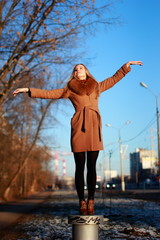 Young woman wearing coat stands on a stand, cold winter day, hands to the side.