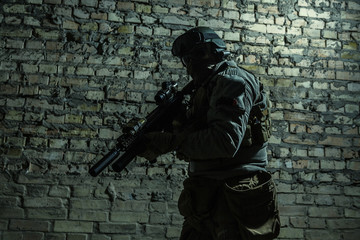 Fototapeta na wymiar Special forces operator pointing weapon in the dark. Combat helmet, and bulletproof vest are on. Low key image, shadow soldier