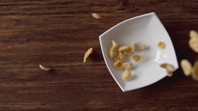 Corn flakes falling in white bowl with copyspace to the left on wooden table