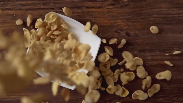 Corn flakes falling in white bowl with copyspace to the right on wooden table